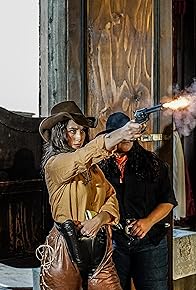 Woman dressed as cowboy, shooting a gun.
